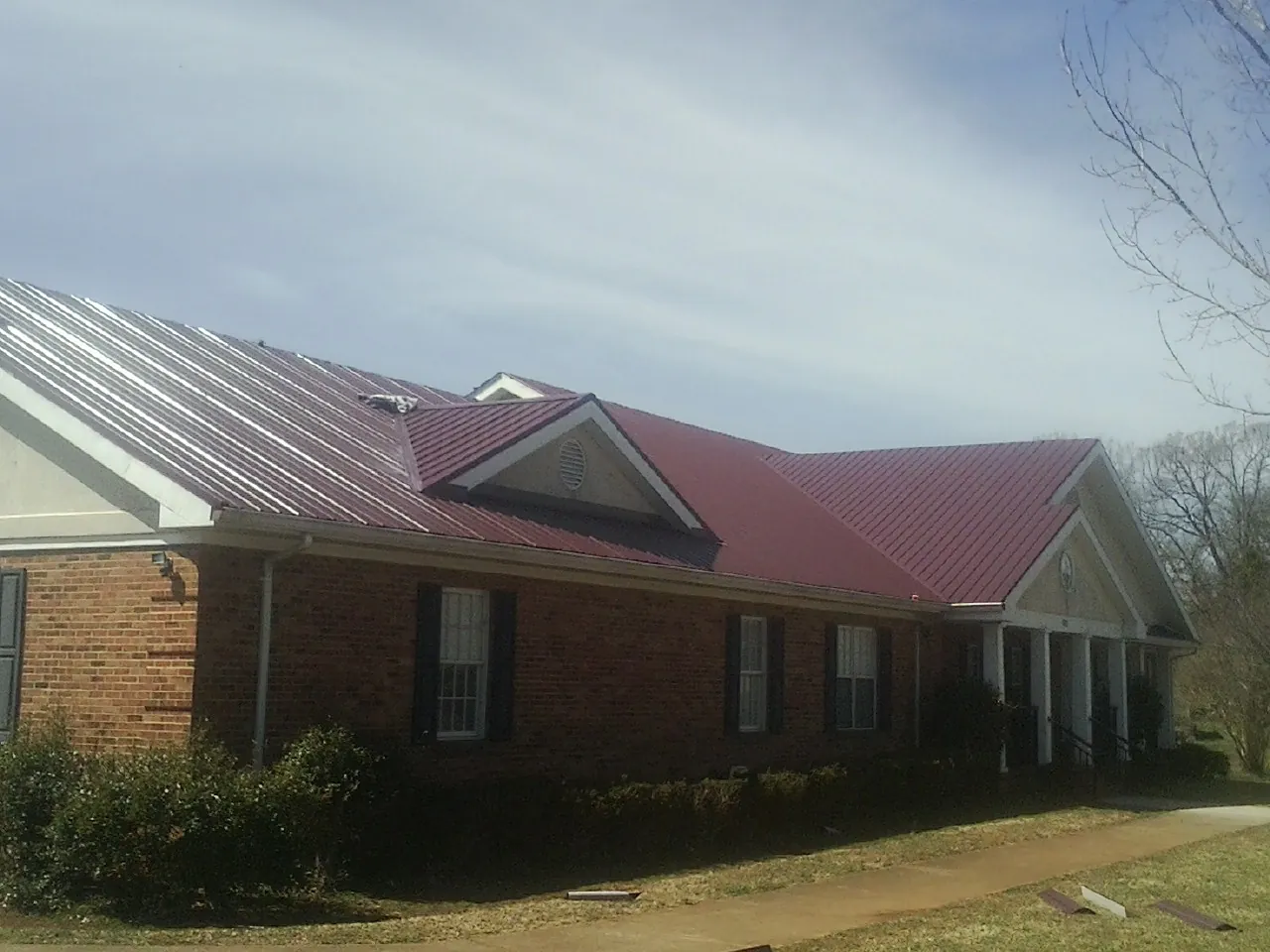 Red metal roof with gabled entries on a long brick building, from a Hail Damage Roof Repair job in Vernon Hills