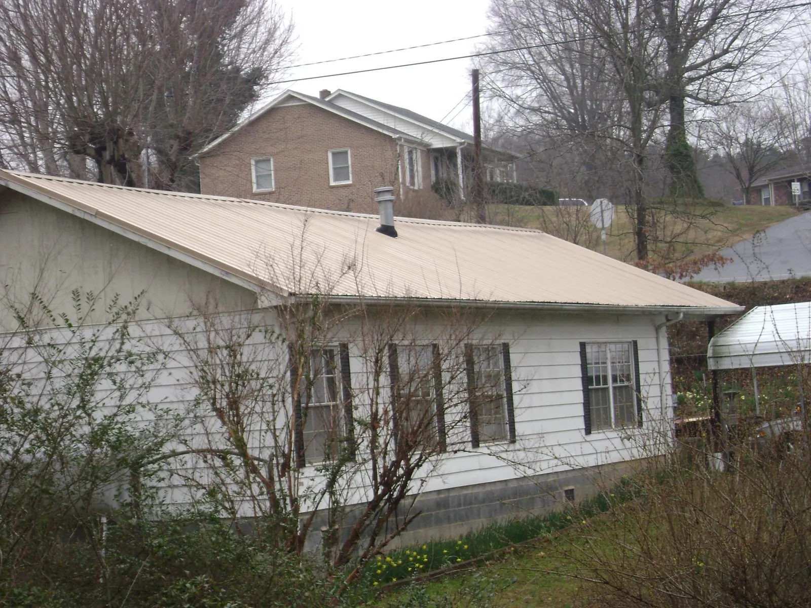 Tan metal roof on a white sided house set into a hillside — Commercial Roofing by Roofing Brothers in Vernon Hills